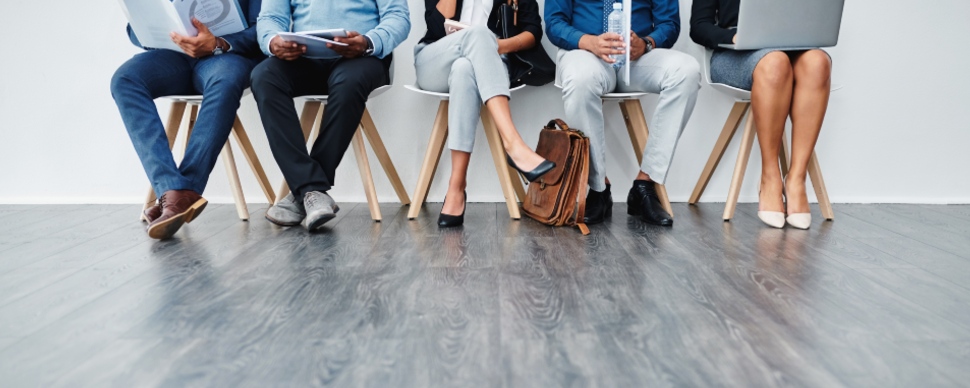 Row of diverse job candidates seated in a waiting area.