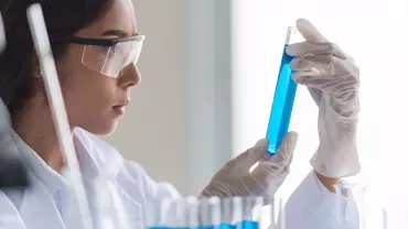 Scientist examining a blue liquid in a test tube.