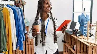 Person smiling and holding a tablet and coffee cup in a clothing store.