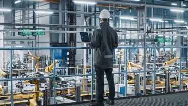 Person in a hard hat observes a factory floor with robotic arms.