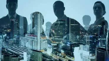 Silhouettes of business people overlaying a cityscape at night.