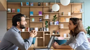 Two people having a conversation at a table in a modern office space.