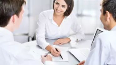 Three people in a meeting smiling and discussing documents.