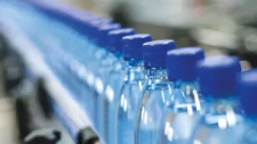 Row of plastic water bottles with blue caps on a conveyor belt.
