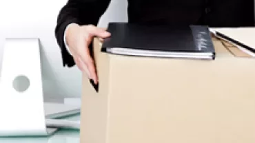 Person holding a folder and a cardboard box filled with items in an office setting.