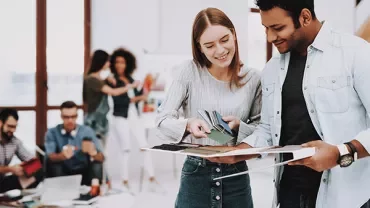 Two people discussing fabric swatches, with a group working in the background.