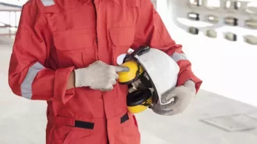 Person in red uniform holding a safety helmet with ear protection.