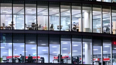 View of a modern office building with large windows showing people working inside.