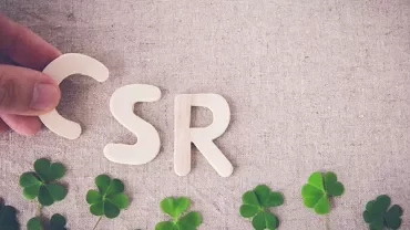 Hand arranging wooden letters C, S, R on fabric with clover leaves.