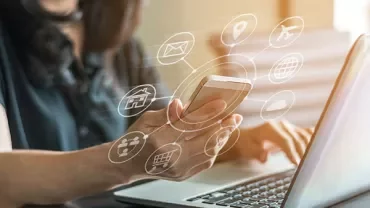 Person using a smartphone and laptop with digital icons surrounding.