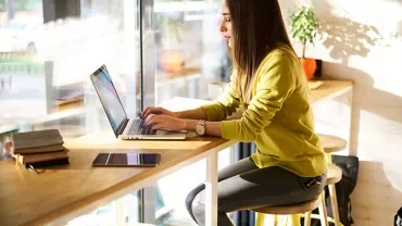 Person sitting at a window-side cafe working on a laptop.