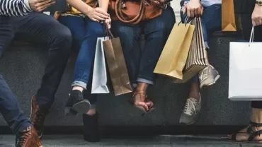 People sitting with shopping bags and using devices.