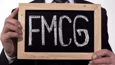 Person holding a small framed chalkboard with 'FMCG' written on it.