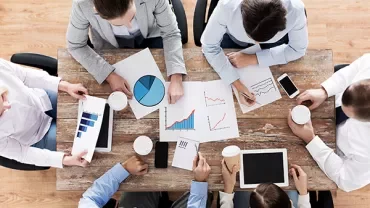 Top view of a team meeting with charts and coffee on a wooden table.