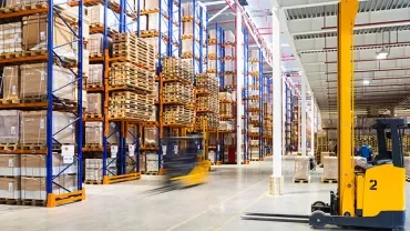 A forklift moves in a large warehouse filled with stacked boxes.