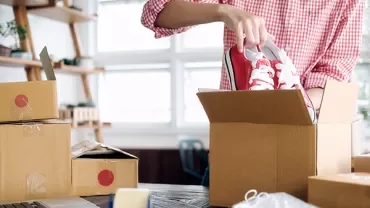 Person packing red sneakers into a cardboard box.