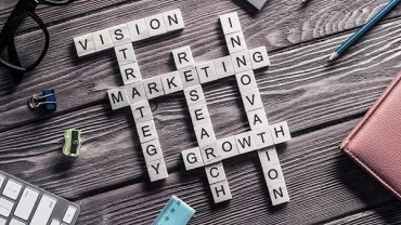 Wooden desk with crossword puzzle spelling business terms: vision, strategy, marketing, research, innovation, growth.
